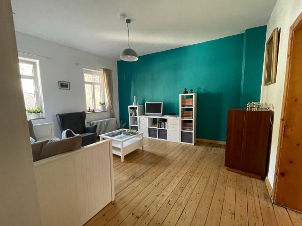 Wohnzimmer mit Fernseher und Musikanlage Heller Wohnraum mit blauer Wand, Sofa, TV und gemütlicher Einrichtung aus Holz und Weiß.