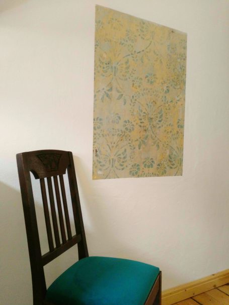 ein Stück erhaltene originale Wandbemalung in der Küche Holzstuhl mit grünem Kissen neben einer Floral tapete an einer Wand.