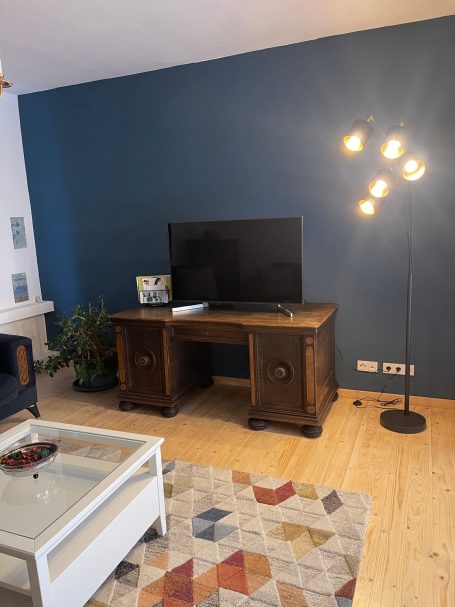 Wohnzimmer mit großem Smart-TV Moderner Wohnraum mit TV, Holzschreibtisch, Stehlampe und buntem Teppich.