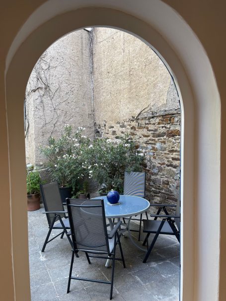Blick von der Küche zum Essbereich auf der Terrasse Gemütlicher Innenhof mit Tisch, Stühlen und Pflanzen, sichtbar durch einen Rundbogen.