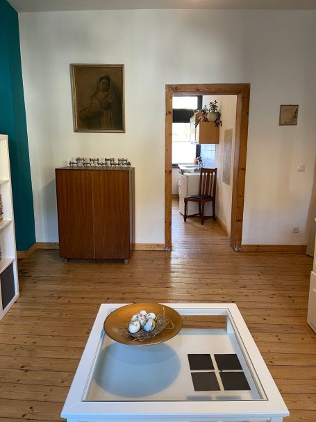 Blick vom Wohnzimmer zur Küche Wohnraum mit Holzboden, blauem Akzent, Möbeln und einem Tisch mit Schale.