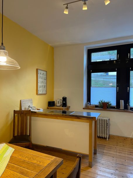 Küche mit Blick auf die Weinberge Helles Zimmer mit Holztisch, Küchenzeile und großen Fenstern.