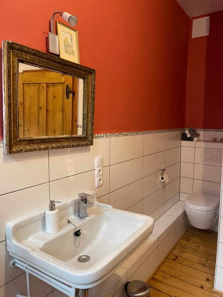 Badezimmer mit Waschbecken und WC Bad mit roter Wand, Waschbecken, Spiegel und WC in moderner Ausstattung.