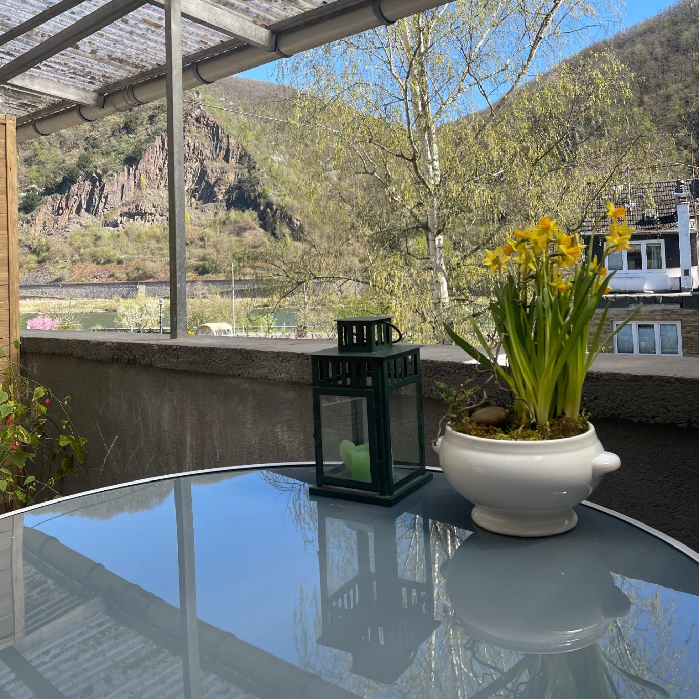 Blühende Blumen in einem Topf und eine Laterne auf einem Tisch mit Ausblick auf Berge.