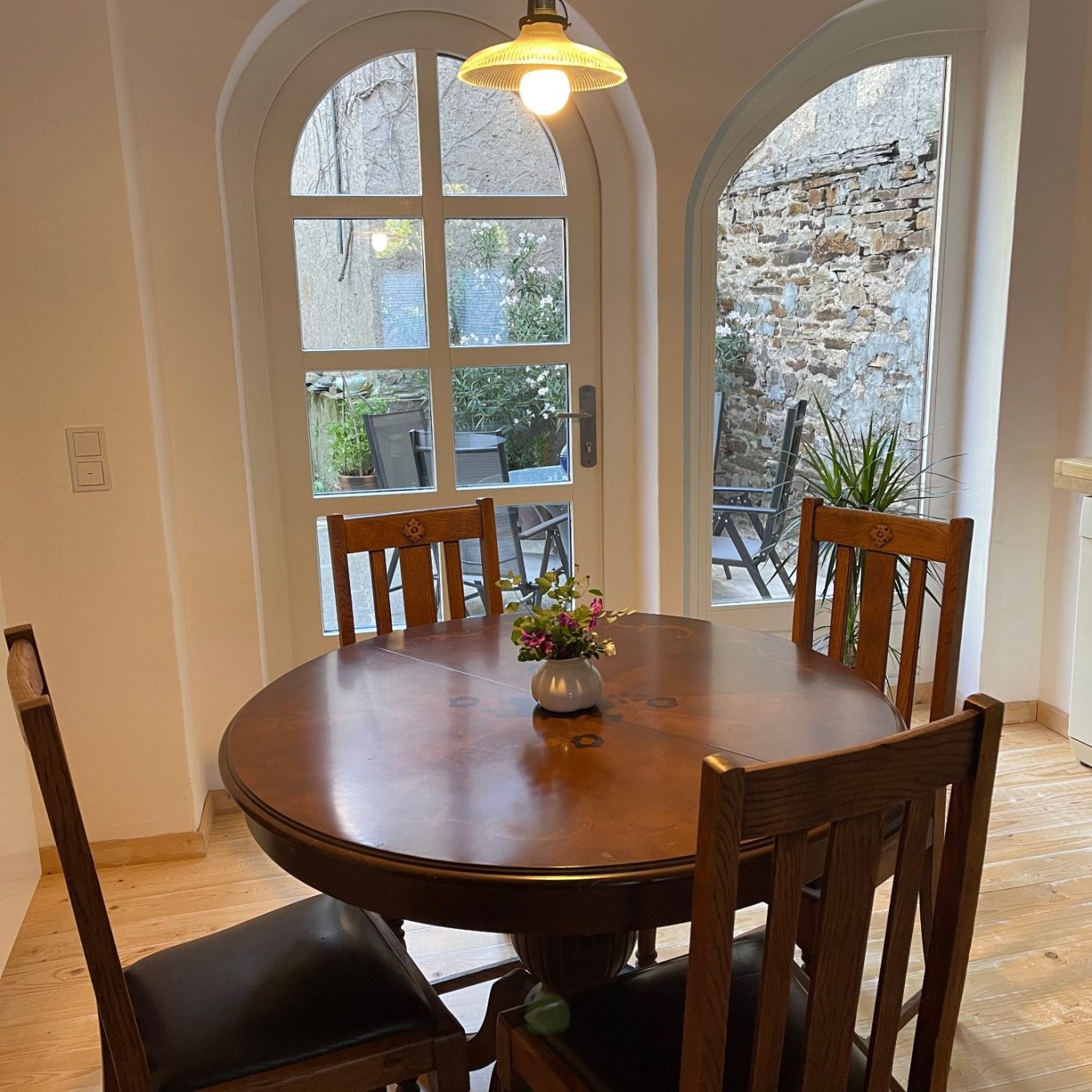 Holztisch mit Stühlen in einem hellen Raum mit Fenstern und Pflanzen.