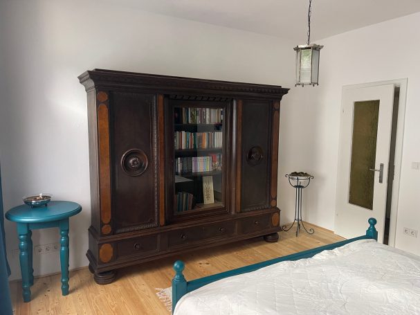 Schlafzimmer mit altem Schrank als Bibliothek und Stauraum Holzschrank in einem modernen Schlafzimmer, daneben ein runder Tisch und eine Lampe.