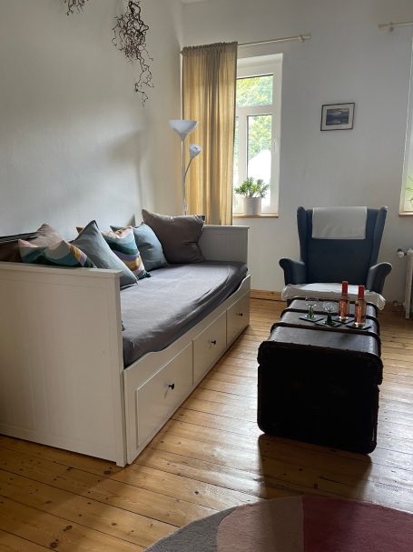 Wohnzimmer mit Schlafsofa Helles Wohnzimmer mit Sofa, Kissen und einem Sessel, dazu ein Tisch mit Kerzen.