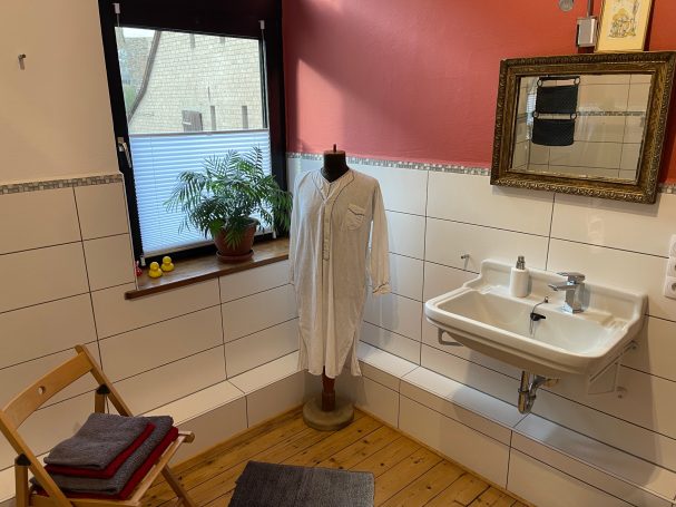 Badezimmer mit Waschbecken und Blick auf die Weinberge Badezimmer mit Waschbecken, Stuhl, Pflanze und einem Kleidungsstück auf einem Standfuß.