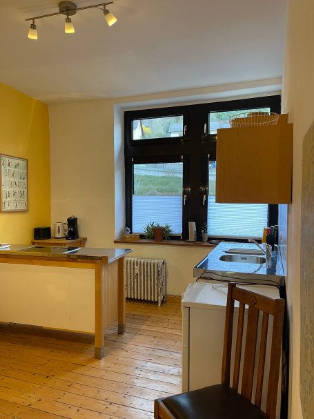 Küche mit Kochinsel, Spüle und Blick auf die Weinberge Küche mit Holzfußboden, gelber Wand, Fensterblick und modernen Geräten.