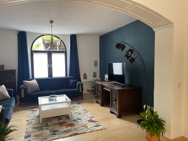 Wohnzimmer mit Smart-TV Wohnzimmer mit blauen Wänden, Sofa, TV und einem bunten Teppich. Stimmungsvolle Beleuchtung.