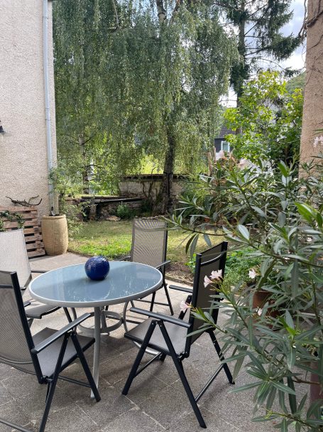 Blick Essbereich auf der Terrasse zum Garten Ein Garten mit einem runden Tisch, vier Stühlen und einer großen grünen Hecke.